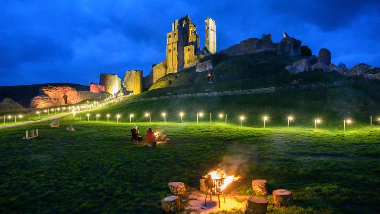 Corfe Castle at dusk with lights and fire pits